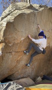 Amy is climbing a rock formation on a sunny day.