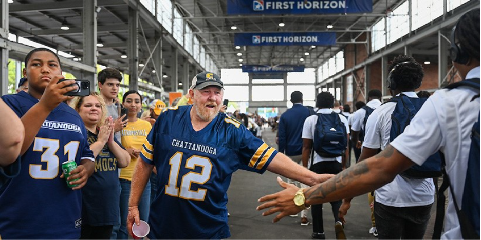 A UTC fan high fives a football player as he walks through the First Horizon Pavillion