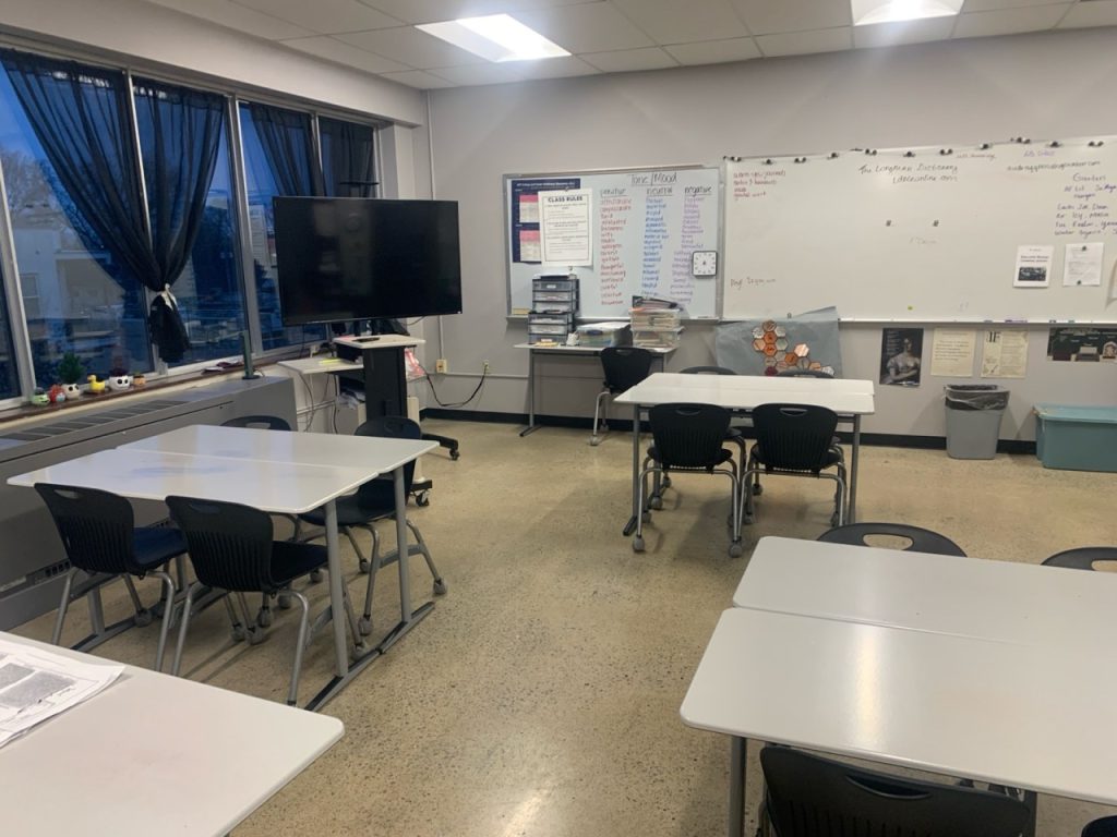 Inside of a classroom at a Chattanooga charter school. Photo of tables where four students sit together, a marker board at the front of the classroom and a large television on a stand.