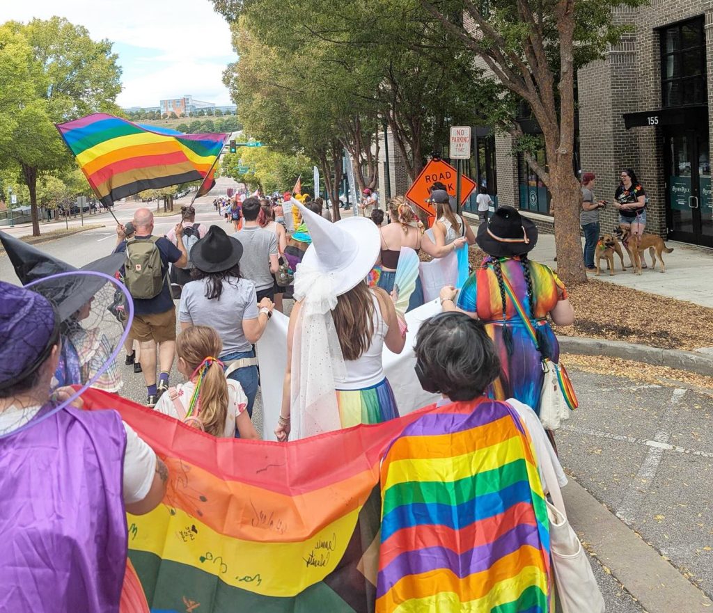 People marching in downtown Chattanooga for October 2025 pride parage. People are waiving pride flags.