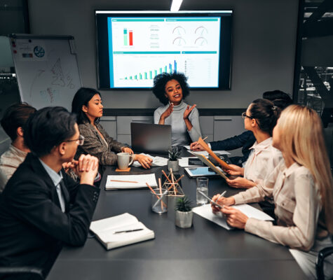 Young confident successful business people discuss and analyze work, statistics, plans, startup in a meeting room with a display screen behind them. Image: HBS]/stock.adobe.com