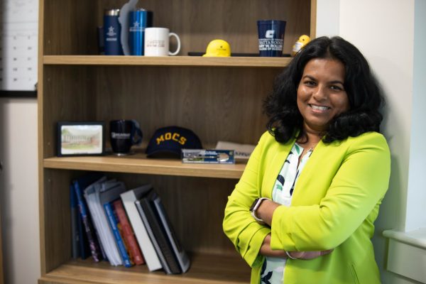 Woman stands in front of a bookshelf smiling with her arms crossed.