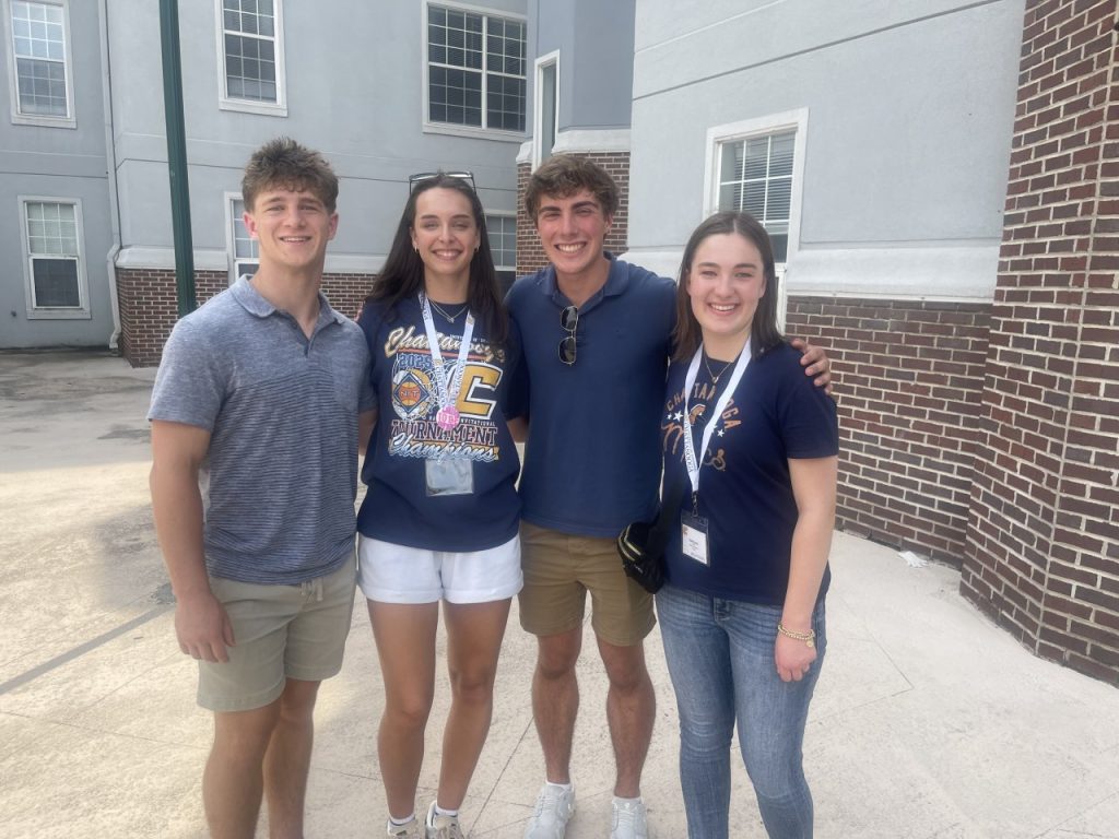 Reagan Macey stands outside a UTC dorm wearing a blue UTC shirt and is surrounded by 3 friends. 