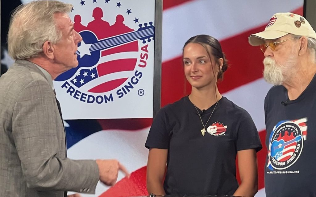 Reagan Macey stands in between two men as she appears on News 12 TV to promote Freedom Sings. 