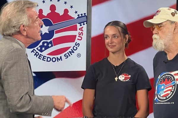 Reagan Macey stands in between two men as she appears on News 12 TV to promote Freedom Sings.
