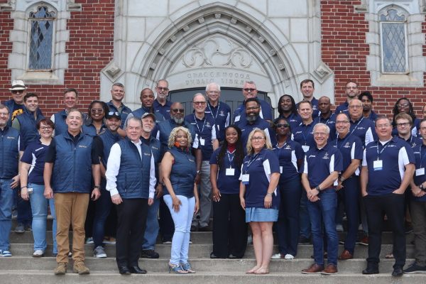 Group of people smiling at camera. They're wearing navy shirts and standing on stairs in front of a brick building.