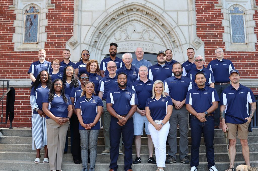 People wearing navy polo shirt standing in front of brick building