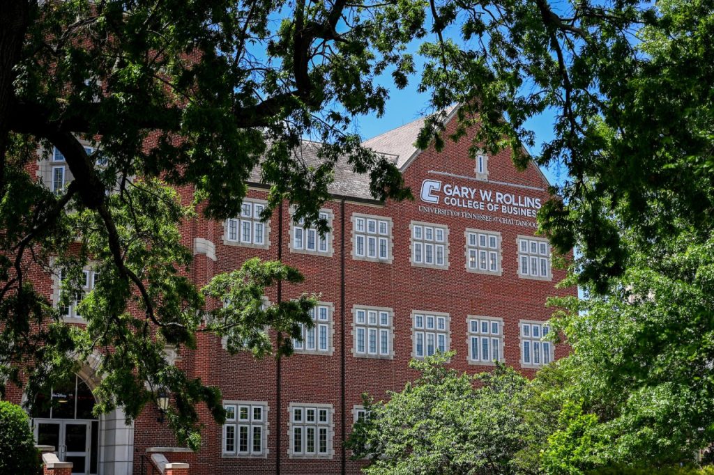 Picture shows the exterior of Fletcher Hall through the trees with the Gary W. Rollins College of Business logo on the side of the building.