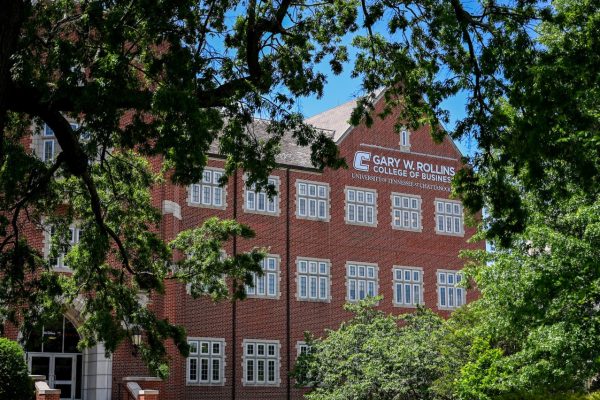 Picture shows the exterior of Fletcher Hall through the trees with the Gary W. Rollins College of Business logo on the side of the building.