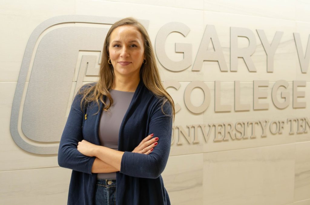 Woman smiling at camera, standing in front of a wall that says Gary W. Rollins College of Business.