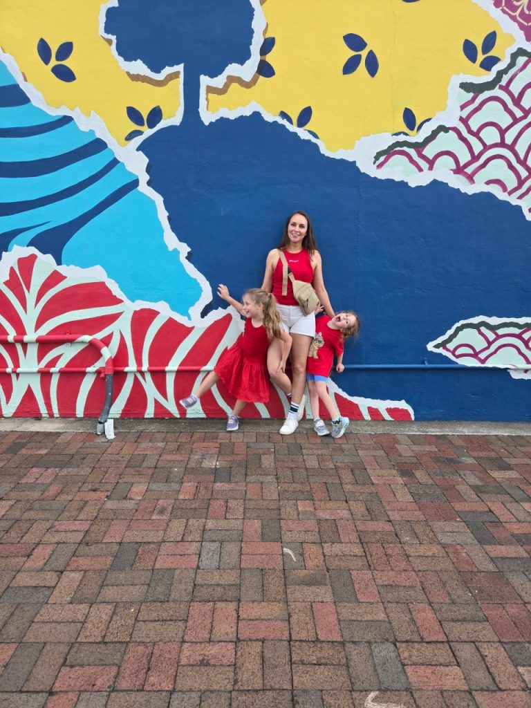 Mom and daughters smile in front of a mural wall