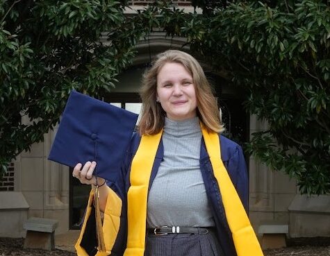 A college graduate poses with their cap and gown.