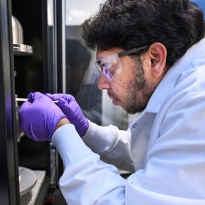 Close-up of Dr. Venkat Kode working with laboratory equipment while wearing safety glasses, gloves and a lab coat during water-harvesting research at UTC.