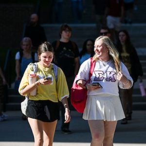 Two girls walking together. One looks at her phone the other is wearing a Sigma Kappa jersey.
