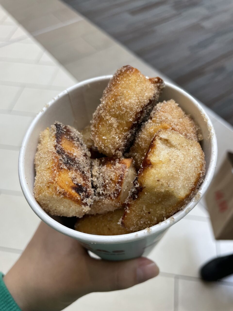 A picture of a hand holding cinnamon pretzels in a cup