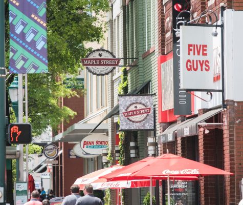 A group of four people walk down Broad Street in downtown Chattanooga, Tenn., surrounded by cafe tables; tall, red brick buildings; and a number of business signs.