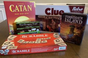 A variety of family board games are displayed: Catan, Scrabble, The Oregon Trail, Clue, and Forbidden Island