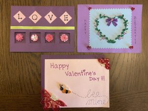 3 of Pato's quilling projects are displayed as holiday cards. One is a purple card that says "Love" with pink flowers. The second card has a large heart formed out of flowers and a bow in the middle. The third card is light pink that says "Happy Valentine's Day--Be mine", except there is a bumble bee to represent the word "Be". 