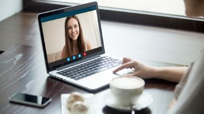 an open laptop with two people videoconferencing and a latte