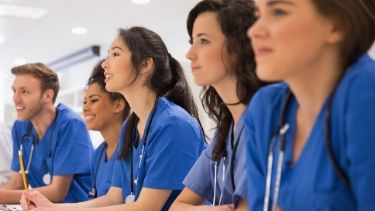 students in blue scrubs listening to an instructor talk