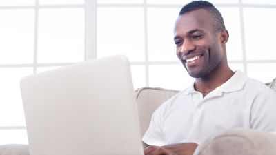 man smiling while typing on his white laptop