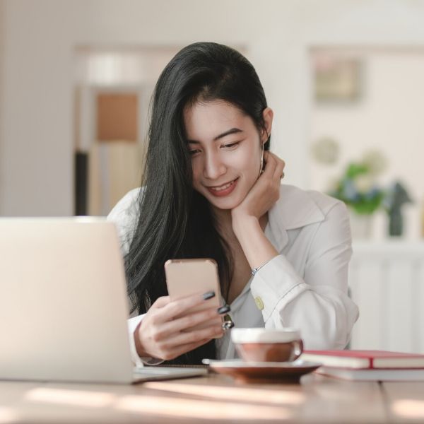 woman smiling looking at her phone by her laptop