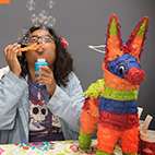 Student blowing bubbles next to a pinata
