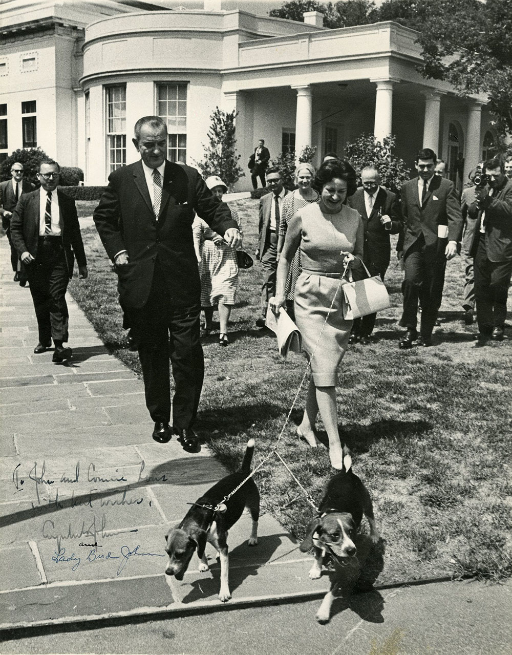 Photograph of President Lyndon B. Johnson and Lady Bird Johnson walking presidential beagles, Him and Her, on the White House lawn.