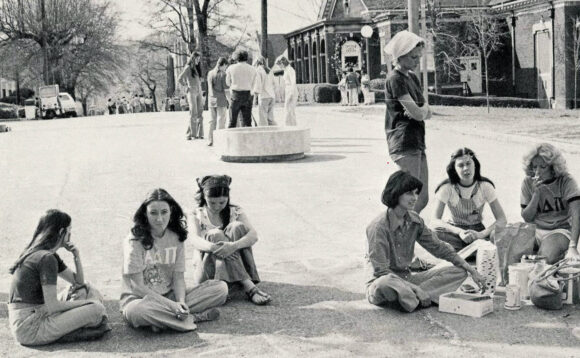 Black-and-white photograph of Sigma Chi Derby participants sitting and standing on Oak Street.
