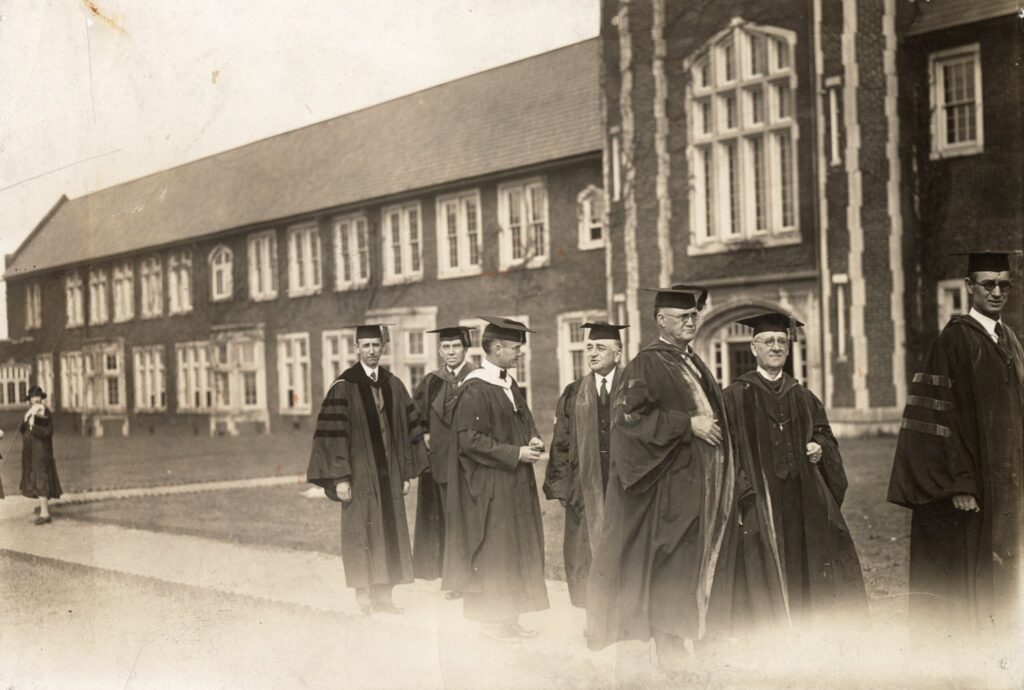 Photograph of University of Chattanooga President Arlo A. Brown and other individuals wearing academic regalia on the quadrangle approaching Patten Chapel.