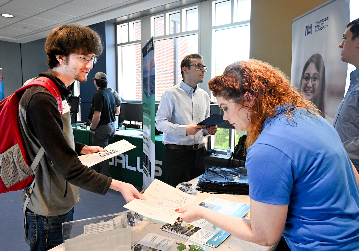 A student passing a piece of paper to a recruiter. 