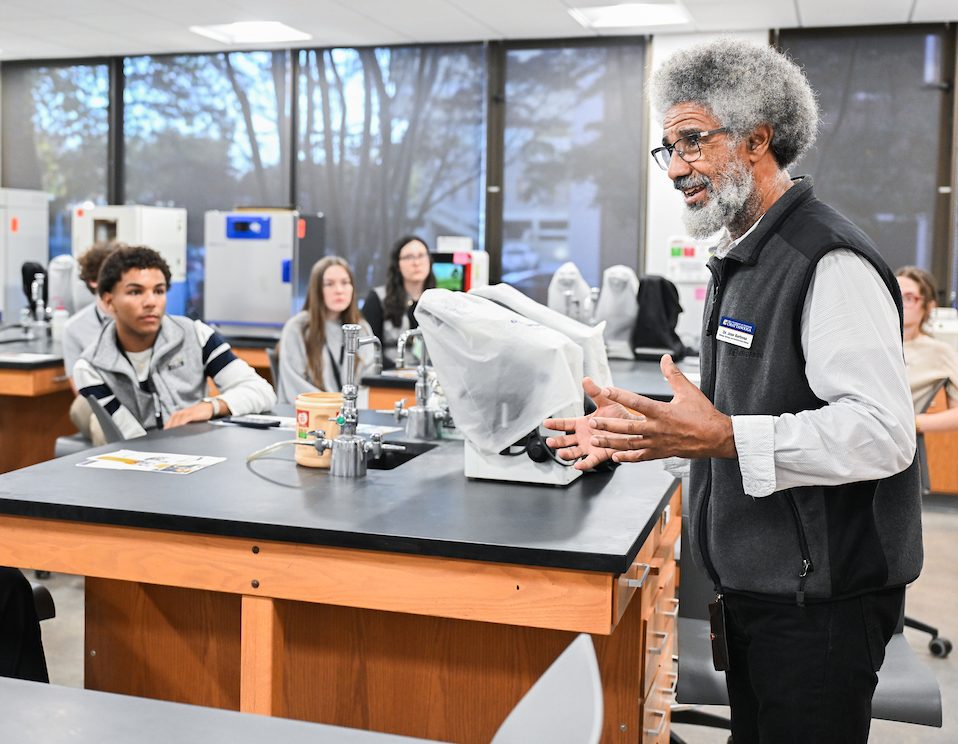 A professor speaks to a group of high school students seated at lab tables during a science demonstration in a UTC laboratory.
