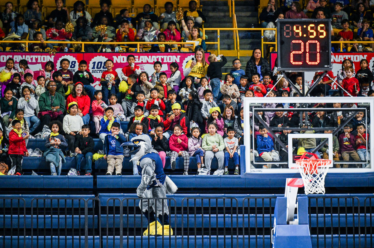 Estudiantes de primaria y secundaria en las gradas, Scrappy y canasta de baloncesto.