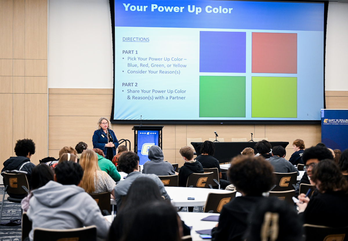 Jackie Morgan stands at the front of a room full of students sitting in chairs, with a PowerPoint presentation behind her.