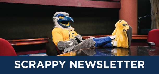 Scrappy mascot relaxing at a table with their legs propped up